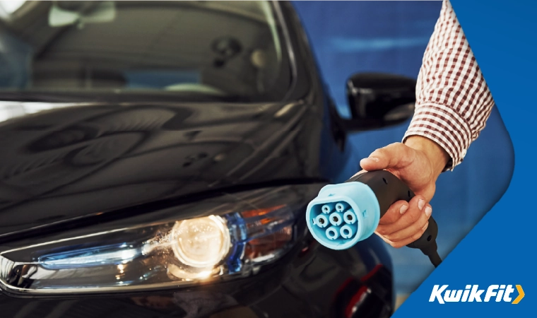 Person holding a electric car charger whilst walking around a black car.